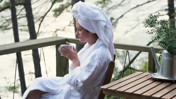 Young Woman in a Bathrobe and Towel on the Terrace on a Background of Mountains and Forest. Woman