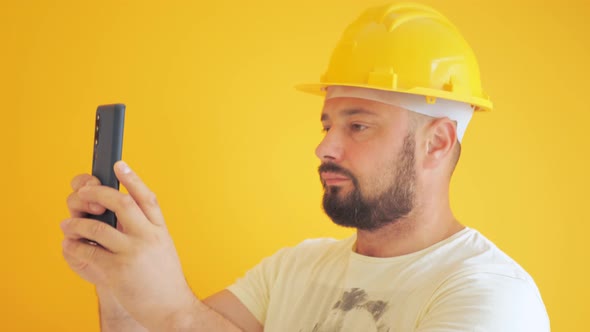 Construction Worker on a Yellow Background Takes a Photo on the Phone