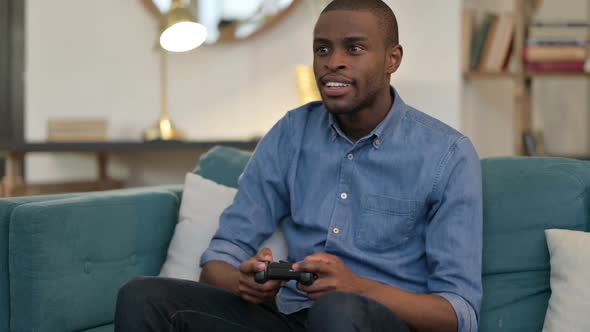 Young African Man Playing Video Game on Sofa