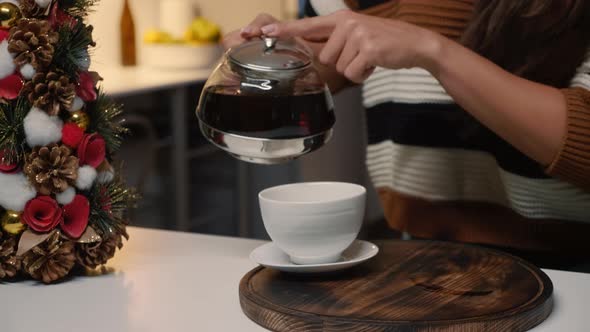 Festive Young Woman Pouring Tea From Kettle in Cup