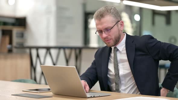 Tired Young Businessman with Laptop Having Back Pain in Office