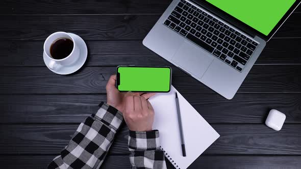 Top View of Female Hands Using Smartphone with Blank Green Screen in Front of Laptop with Chrome Key