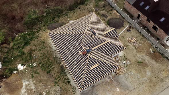 Aerial view of unfinished brick house with wooden roof frame structure under construction.