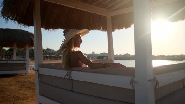 Woman sitting at Cabana with straw roof on a sandy beach on sunset