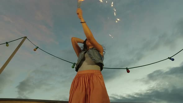 Under view of brunette woman jumping with firework candle on the rooftop terrace