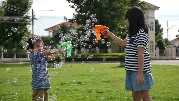 Cute Asian Children Shooting Bubbles From Bubble Gun In The Park