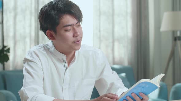 Close Up Of Asian Man Student Reading A Book While Studying At Home