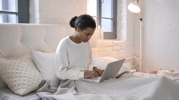 Shocked Young African Girl Wondering to Results on Laptop in Bed