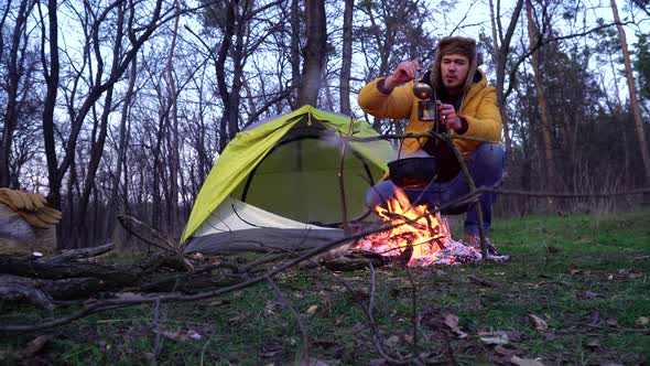 The Guy Prepares Food Near a Campfire and a Tent in the Woods