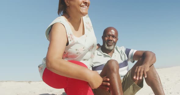 Smiling senior african american couple embracing and looking at sea on sunny beach