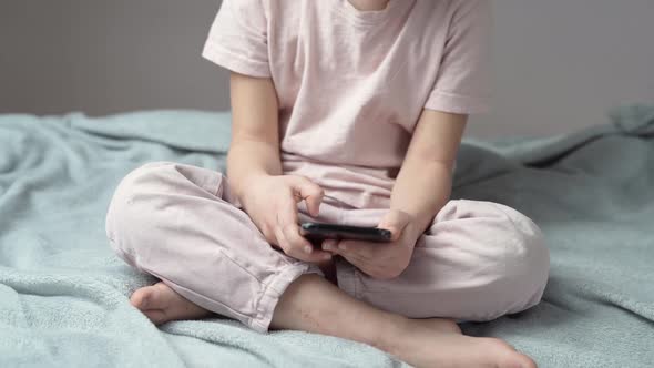 Girl sitting cross-legged on bed playing game on smartphone