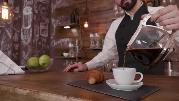 Gently Poring a Cup of Fresh Brewed Coffee on a Tray with a Croissant