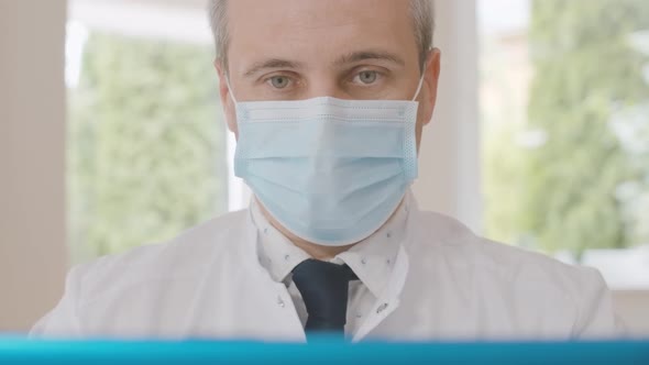 Close-up of Mid-adult Doctor in Face Mask Talking at Laptop Selfie Camera. Portrait of Confident