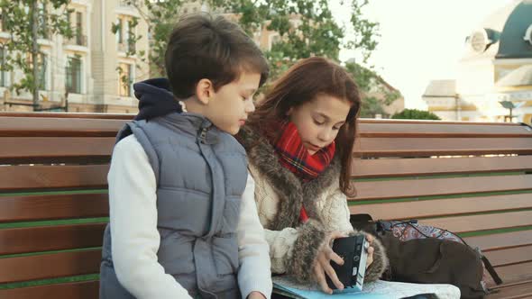 A School Girl and Her Friend Sit on a Bench and Examine the Camera