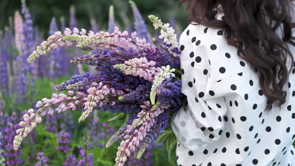 Young Beautiful Woman Posing in a Field with a Bouquet of Lilac Flowers. Happy Brunette in a Field