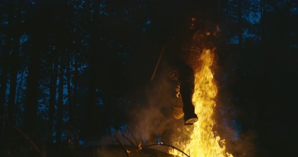 Fire Fighter with Safety Equipment and Axe Extinguishing Fire in Forest at Night