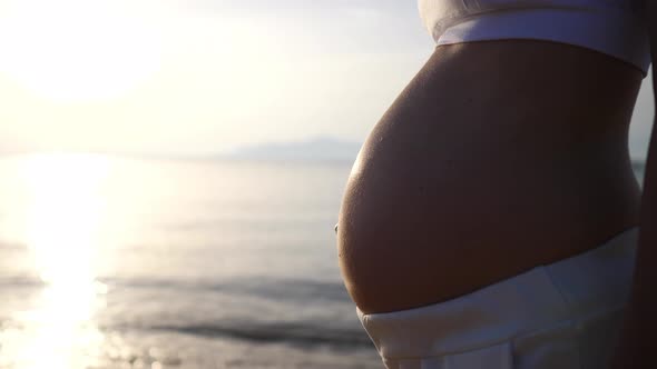 Close Up of Baby Bulb Pregnant Woman with Big Belly Posing on the Sunny Sea Coast Enjoying Sunbeams