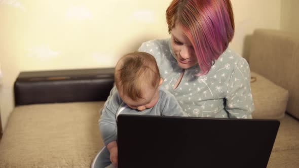 Mother is Working From Home Sitting in Front of Laptop with Baby Son on Her Knees