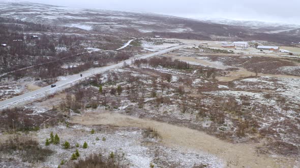 Snowfall At Dovre With Vehicle Traveling Along Fields With Trees In Wintertime In Norway. - aerial