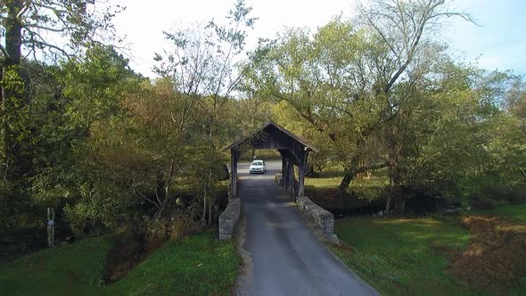 White automobile drives through a wooden covered bridge in the country.