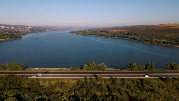 the Flight of the Drone Over a Highway with Moving Cars and a Lake in the Suburbs