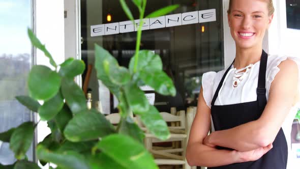 Portrait of smiling waitress standing with arms crossed