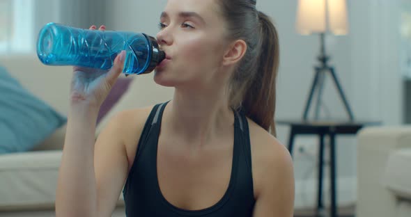 Sporty Woman Drinking Water and Use Phone While Resting After Training at Home. Healthy Lifestyle