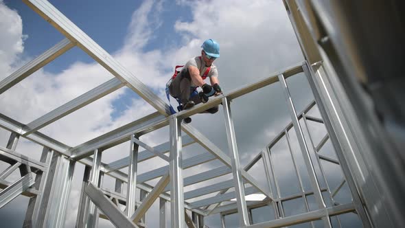Safety Harness Equipment. Caucasian Contractor in His 30s on a Steel Building Frame alt
