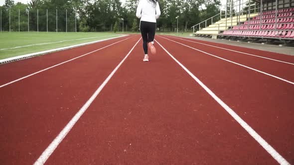 Young woman is running in the stadium. woman with white sweater and black tights. Camera tilts up.