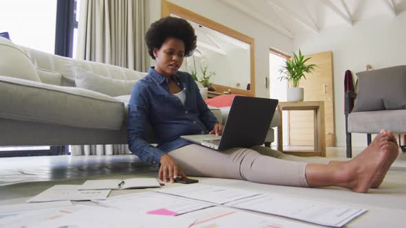 Happy african american woman sitting on floor, using laptop and working