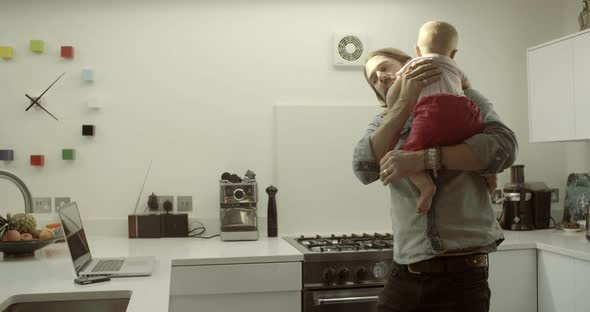 Father carrying daughter and using laptop in kitchen