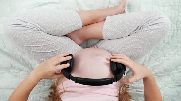 Top View of Pregnant Woman Putting Headphones and Stroking Her Big Belly