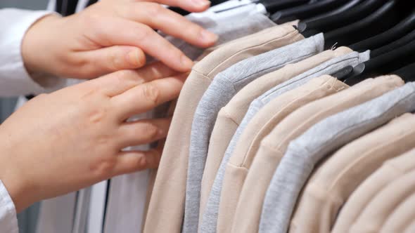 Female Hands Sort Cotton Pullovers on a Hanger in a Clothing Store