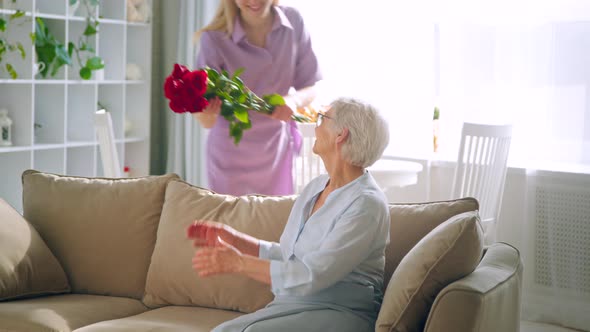 Young girl gives flowers to aged lady with joyful smile at birthday