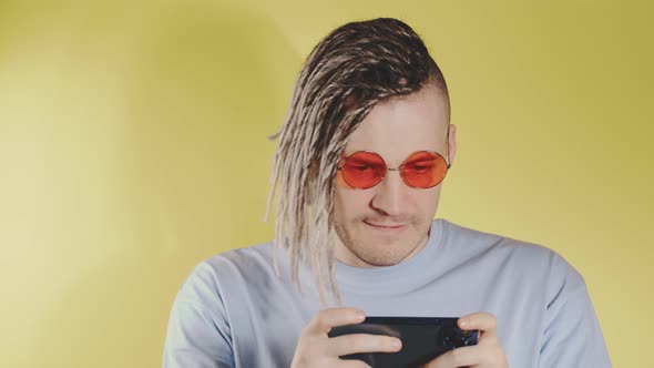 Young enthusiastic man with dreadlocks playing on smartphone.