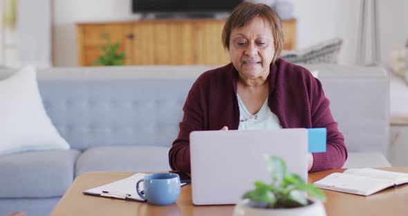 Happy african american senior woman at dining table, making video call using laptop and talking