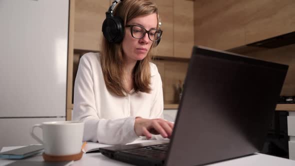 Woman in Headphones Makes Notes in Notebook While Listening Online Course at Laptop