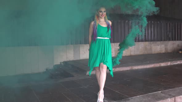 Cute Girl in a Green Dress with African Braids and Colorful Makeup Posing with Bright Green Smoke on
