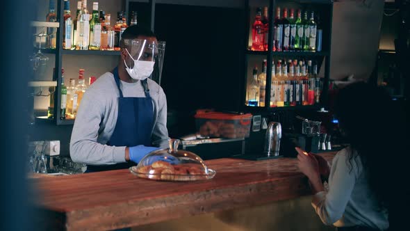 African Barista in a Face Mask Accepts NFC Payment From a Lady