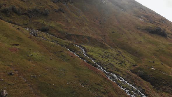 Dramatic turn along a Scottish hillside to center on a stream of mountain water rushing downhill in