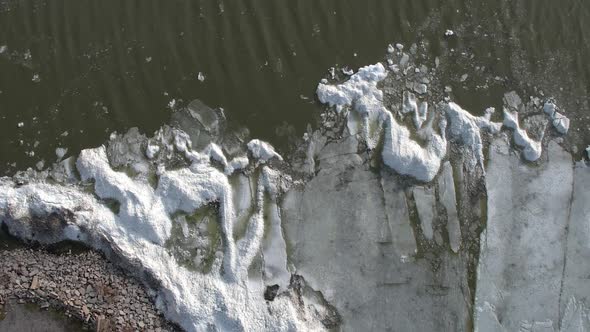 Aerial high above edge of lake looking down at piles of ice