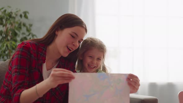 Joyful Teenage Girl and Sister Look at Painting in Apartment