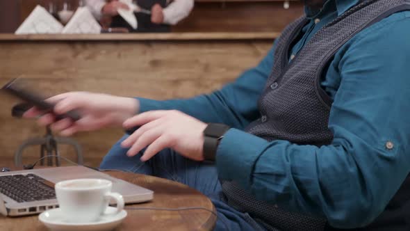 Freelancer in a Pub Finishes a Phone Conversation and Starts Typing on His Laptop