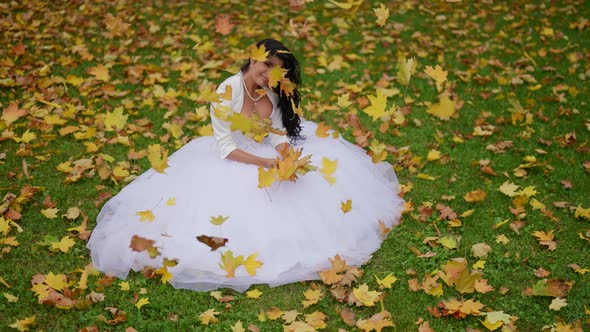 Beautiful Bride in Autumn Day Sitting on Grass with Yellow Maple Leaves Happy Woman
