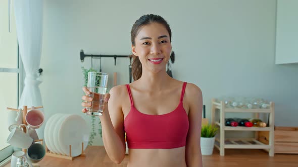 Asian beautiful active sport woman in sportswear drink water after exercise in kitchen in house.