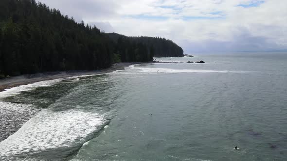 Surfers looking for the perfect wave at Sombrio Beach on a slightly cloudy spring day in Canada. Aer