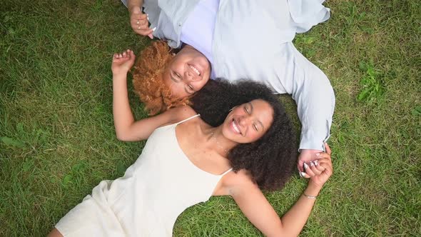 Young Beautiful Happy Lesbian African American Couple Lying on Grass Laughing Stretching Out Hands