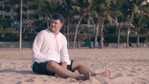 Tourist in Cap Sits and Looks Aside on Clean Coast Sand