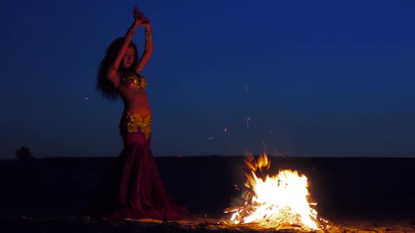 Curly Brunette Dancing Belly Dance Near the Fire, in the Background Sunset