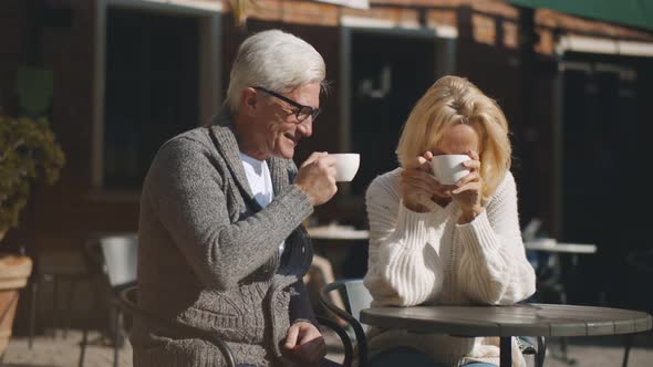 Happy Mature Couple Enjoying Coffee and Smiling While Sitting on Cafe Terrace